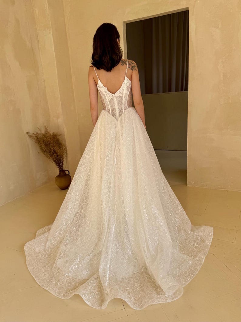 May include: A white wedding dress with a lace bodice and a flowing skirt. The dress has a low back and a fitted bodice.