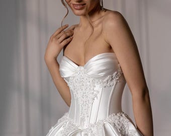 May include: A strapless white satin wedding dress with a sweetheart neckline and a fitted bodice. The bodice is embellished with intricate beadwork and lace detailing. The skirt flares out from the waist, creating a full, elegant silhouette.