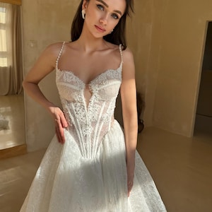 May include: A white lace wedding dress with a fitted bodice and a flowing skirt. The bodice has a sweetheart neckline and a lace-up back. The skirt is made of layers of tulle and has a slight train.