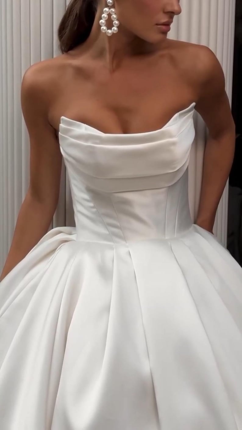 May include: A white strapless satin wedding dress with a fitted bodice and a flowing skirt.