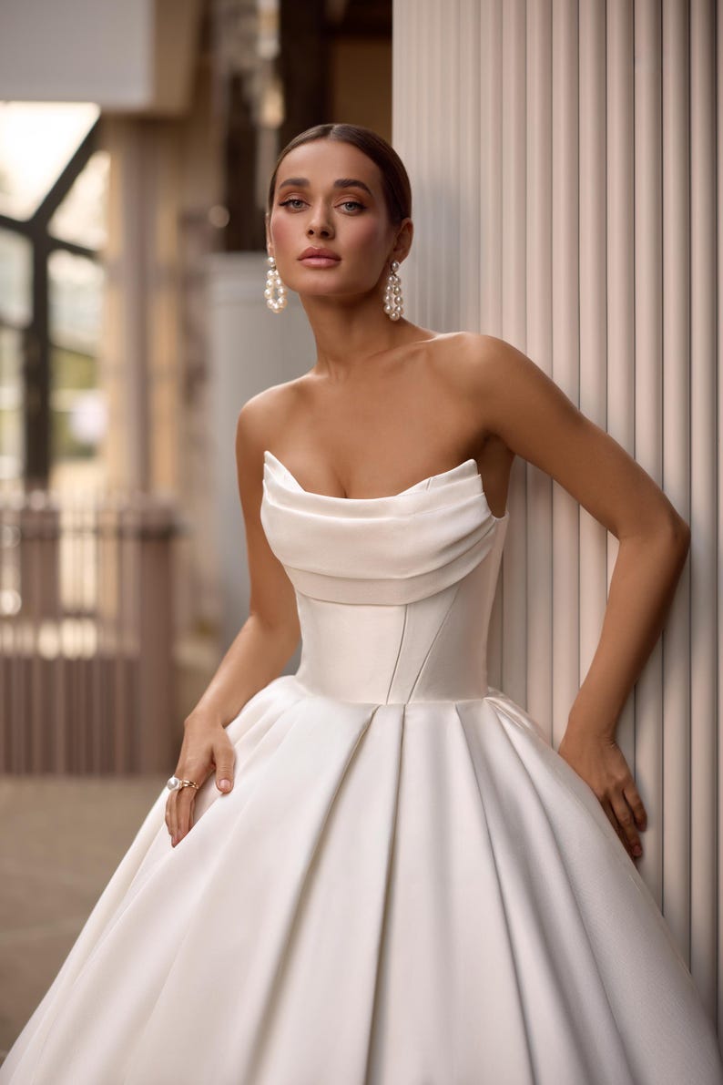 May include: A white strapless satin wedding dress with a fitted bodice and a flowing skirt.