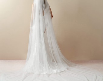May include: A long, white bridal veil made of tulle with a scalloped edge. The veil is draped over a person's head and shoulders, and the train extends to the floor.