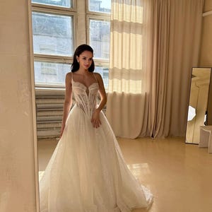 May include: A white wedding dress with a lace bodice and a flowing skirt. The dress has a sweetheart neckline and a fitted bodice. The skirt is full and has a slight train.