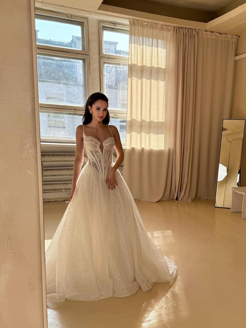 May include: A white wedding dress with a lace bodice and a flowing skirt. The dress has a sweetheart neckline and a fitted bodice. The skirt is full and has a slight train.