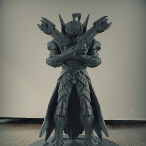 Op de afbeelding: Een grijs 3D-geprint beeldje van een skeletkrijger met een schedelvormige helm en een cape. De krijger houdt twee wapens in gekruiste positie. Het beeldje staat op een ronde basis.