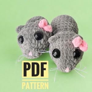 May include: Two grey crocheted plush mice with large black plastic eyes, small pink noses, and pink yarn bows on their heads. Each mouse features thin white whiskers. A yellow square graphic with the black text PDF PATTERN is visible.