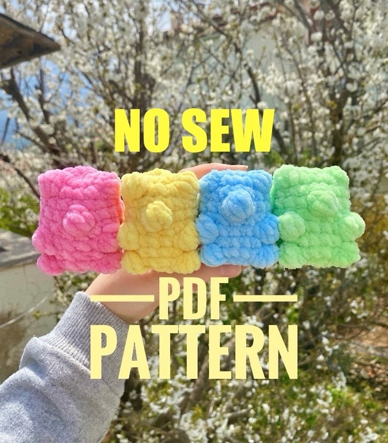 May include: Four crocheted teddy bears in pink, yellow, blue, and green. The bears are held in a hand with the text "NO SEW - PDF PATTERN" displayed below.
