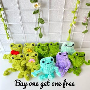 May include: A group of 10 crocheted frog plushies in various colors, including green, blue, purple, and pink. The frogs are arranged in a circle on a white background. The text "Buy one get one free" is written below the frogs.