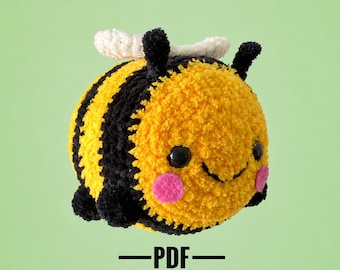 May include: A round, crocheted bee plush toy with yellow and black stripes, white wings, black antennae, and pink cheeks. The bee has black safety eyes and a stitched smile. Below the bee, the text reads PDF PATTERN in black capital letters.