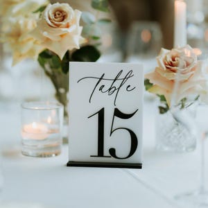 May include: White acrylic table number with black text. The number is 15. The text reads "Table".