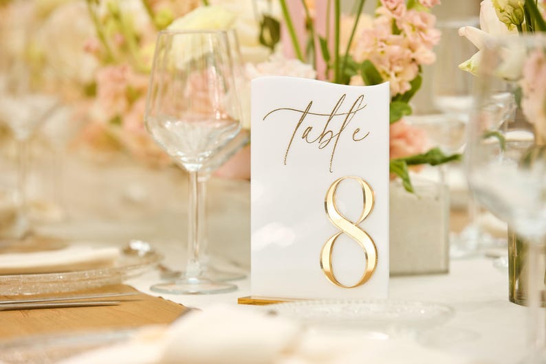 May include: White table number card with gold lettering that says "Table" and the number "8".