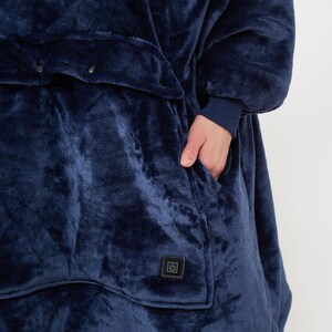 Puede incluir: Una manta port&aacute;til azul marino con una textura suave y aterciopelada. Cuenta con un bolsillo frontal grande y un s&iacute;mbolo de bot&oacute;n de encendido. Los pu&ntilde;os de las mangas son de un tono azul m&aacute;s oscuro.