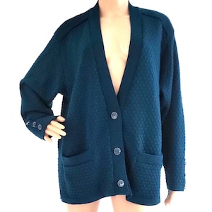 May include: A dark teal button-down cardigan with a textured, quilted pattern. The long-sleeved sweater has two front pockets and buttons down the front. The sleeves have button details at the cuffs.