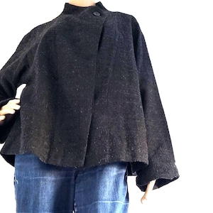 Peut inclure: Veste texturée gris foncé avec un col montant et une fermeture à bouton unique. La veste a des manches larges et une forme légèrement évasée. Elle est associée à un jean en denim bleu. Le style général est moderne et minimaliste.