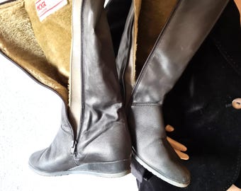 Puede incluir: Un par de botas negras de cuero hasta la rodilla con tacón de cuña. Las botas tienen cierre de cremallera y un cálido forro tipo piel. La marca "HOGL" es visible en una etiqueta.