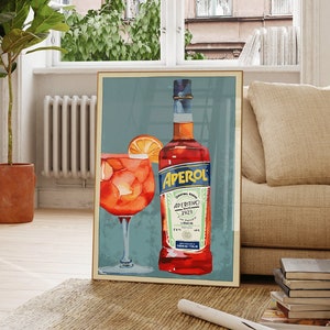 K&ouml;nnte beinhalten: Ein gerahmtes Poster mit blauem Hintergrund, auf dem eine Flasche Aperol Aperitivo und ein Glas Aperol Spritz zu sehen sind. Das Poster h&auml;ngt an einer wei&szlig;en Wand in einem Raum mit Holzboden und einem Fenster.