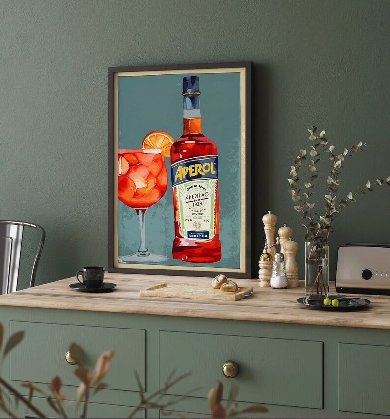 K&ouml;nnte beinhalten: Ein gerahmtes Vintage-Poster mit einer Flasche Aperol Aperitivo Lik&ouml;r und einem Glas Aperol Spritz. Das Poster hat einen blauen Hintergrund mit einem roten und wei&szlig;en Etikett auf der Flasche.