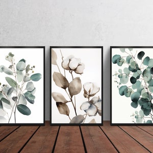 May include: Set of three framed watercolor prints featuring botanical illustrations of eucalyptus leaves and cotton blossoms. The prints are in shades of green, brown, and white.
