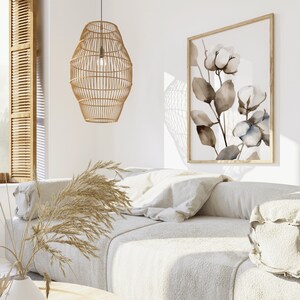 May include: A white couch with a woven rattan pendant light hanging above it. The couch has a few pillows and a throw blanket. A framed print of watercolor flowers hangs on the wall behind the couch.