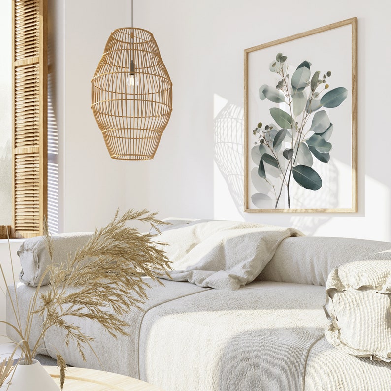 May include: A white couch with a woven light fixture hanging above it. The couch has a throw pillow and a decorative pillow. A framed print of green leaves hangs on the wall behind the couch.