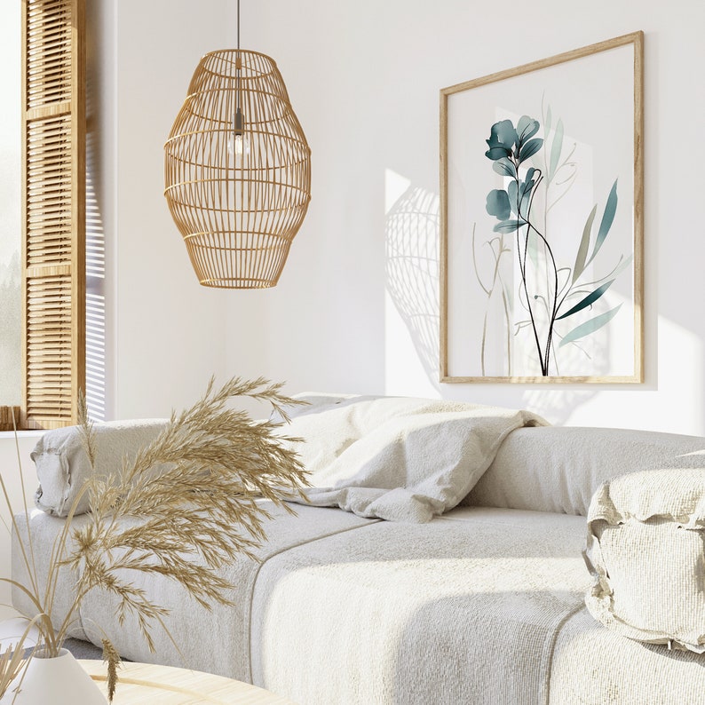 May include: A white couch with a woven wicker pendant light hanging above it. The couch has a throw pillow and a decorative pillow. A framed print of a blue watercolor flower hangs on the wall behind the couch.