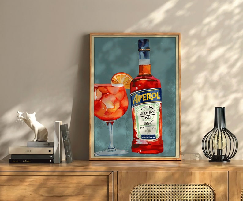 K&ouml;nnte beinhalten: Eine Illustration im Vintage-Stil einer Flasche Aperol Aperitivo und einem Glas Aperol Spritz. Die Flasche ist rot mit einem wei&szlig;en Etikett und dem Text "Aperol Aperitivo 1919" darauf. Das Glas ist mit einer leuchtend orangenen Fl&uuml;ssigkeit gef&uuml;llt und hat eine Orangenscheibe am Rand.