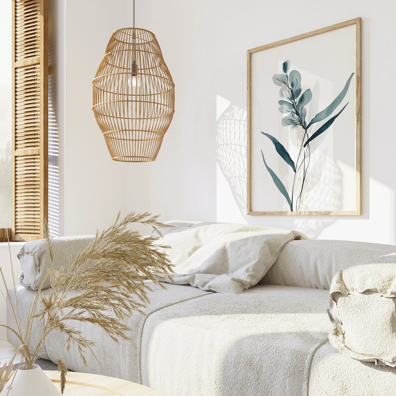 May include: A white couch with a woven wicker pendant light hanging above it. The couch has a throw pillow and a decorative pillow. A framed print of a blue watercolor floral design hangs on the wall behind the couch.
