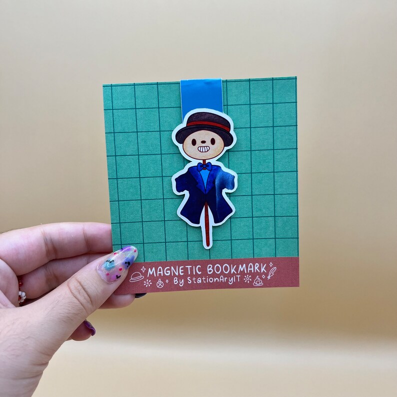 May include: A blue and white magnetic bookmark featuring a cartoon scarecrow with a top hat and a bow tie. The bookmark has the text "MAGNETIC BOOKMARK" and "By StationaryArt" on it.