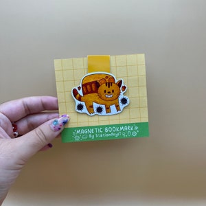 May include: A yellow and brown cat bookmark with black spots and the text "MAGNETIC BOOKMARK By StationaryIT" on a yellow and green background.