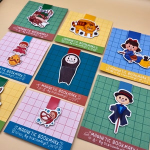 May include: Set of ten colorful magnetic bookmarks featuring various illustrations, including a Totoro character, a creature from the sea, a cat, a girl with a basket, and a scarecrow. Each bookmark has the text "Magnetic Bookmark by StationAryIT" printed on it.