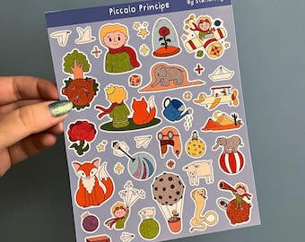 Op de afbeelding: Een vel stickers met illustraties uit De Kleine Prins, waaronder de prins, een vos, een roos, een vliegtuig en een slang. De stickers zijn op een lichtblauwe achtergrond en hebben een witte rand. De tekst "Piccolo Principe" en "By StationaryArt" staat bovenaan het vel gedrukt.