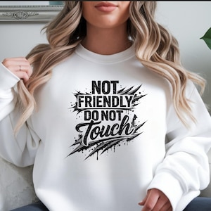 May include: White sweatshirt featuring the black text "NOT FRIENDLY DO NOT TOUCH". The design includes distressed elements, claw marks, and ink splatters. This casual, long-sleeved garment is a statement piece.