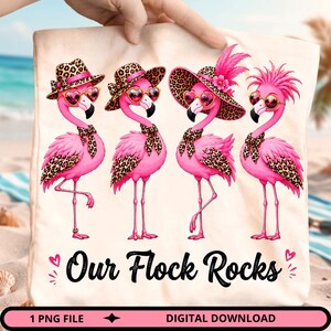 Peut inclure: Un sac fourre-tout de couleur claire orné de quatre flamants roses vifs portant des accessoires à imprimé léopard, des lunettes de soleil en forme de cœur et des chapeaux. Le texte "Our Flock Rocks" est imprimé en noir sous les flamants.