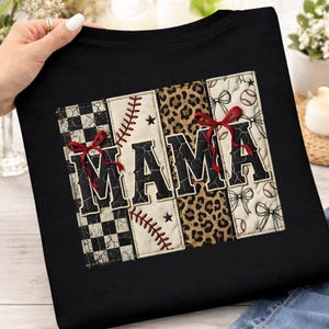 May include: Black sweatshirt with the word "MAMA" in a patchwork design. The letters are decorated with baseball stitching, leopard print, bows, and a checkered pattern. Red bows accent the letters.