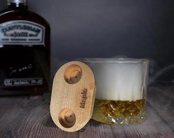 May include: A wooden coaster with two circular cutouts, labeled "Maple". The coaster is oval-shaped and has a light brown color.