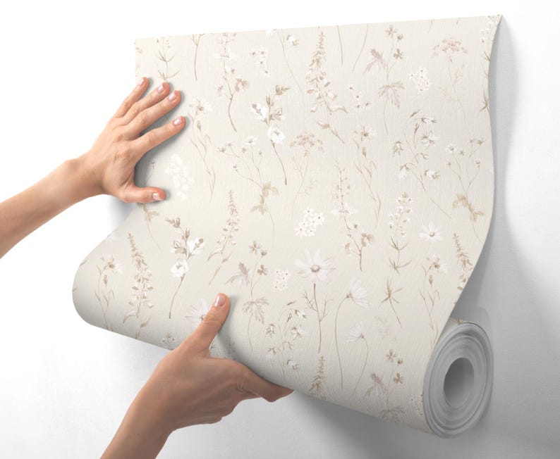 May include: A roll of beige wallpaper with a delicate floral pattern featuring white and brown wildflowers. The wallpaper is being applied to a white wall.