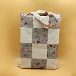 Könnte beinhalten: Eine Patchwork-Tragetasche mit einem karierten Muster aus weißem und floralem Stoff. Die Tasche hat zwei Stoffgriffe.