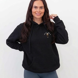 May include: Black hoodie with a front pocket and drawstring hood. The hoodie has a small graphic on the upper left chest that says "Split the G". The person in the image is wearing blue leggings.
