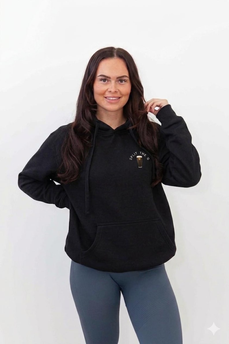 May include: Black hoodie with a front pocket and drawstring hood. The hoodie has a small graphic on the upper left chest that says "Split the G". The person in the image is wearing blue leggings.