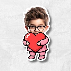 May include: A sticker featuring a cartoon illustration of a child wearing glasses and a pink outfit, holding a large red heart. The child has brown hair and the sticker has a white border.