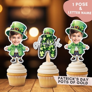 Könnte beinhalten: Drei Cupcakes mit Dekorationen zum Thema St. Patrick's Day. Zwei Dekorationen zeigen einen Cartoon-Jungen in einem grünen Kobold-Outfit und -Hut. Die dritte Dekoration ist ein grüner Buchstabe "A" mit einem Kleeblattmuster und dem Namen "Amanda". Die Cupcakes stehen auf einer Holzoberfläche.