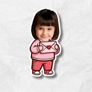 May include: A sticker featuring a cartoon illustration of a young child holding a pink envelope with a heart. The child is wearing a pink long-sleeved shirt and red pants with white stripes. The sticker has a white border.