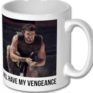 May include: White ceramic coffee mug featuring a black and white image of a man in a gladiator costume. The text "I will have my vengeance" is printed on the bottom of the mug.
