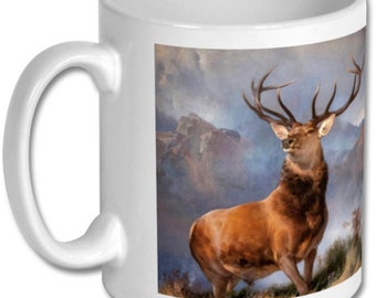 May include: White ceramic mug featuring a colourful image of a red deer with large antlers standing in a mountainous landscape. The deer is facing the viewer and has a brown body with a white chest.