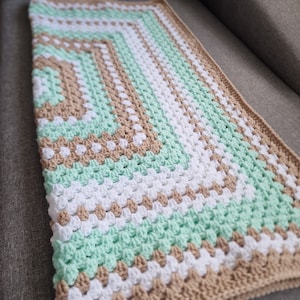 May include: A crocheted baby blanket with a green, white, and brown striped pattern. The blanket is made with a textured stitch that creates a raised, bumpy surface.