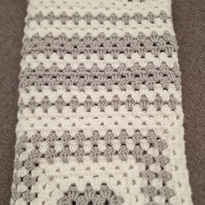 May include: A crocheted baby blanket with a white and gray diamond pattern.
