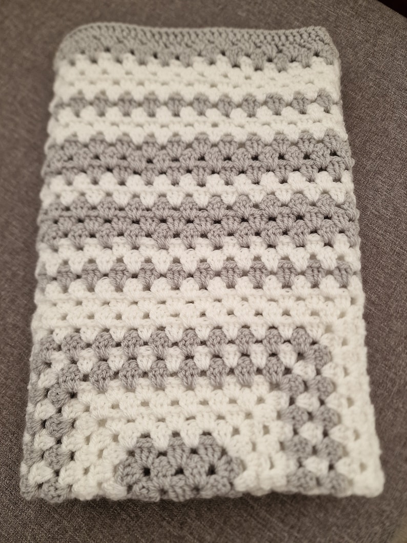 May include: A crocheted baby blanket with a white and gray diamond pattern.