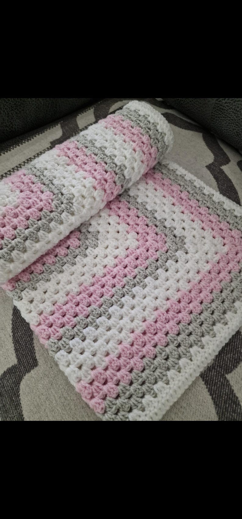 May include: A crocheted baby blanket with pink, white, and gray stripes. The blanket is made with a textured stitch and is folded in half.