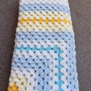 May include: A crocheted baby blanket in shades of blue, white, and yellow. The blanket is made with a granny square pattern and has a diagonal stripe design.