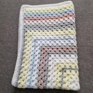 May include: A crocheted baby blanket with a white background and stripes of light blue, yellow, pink, and gray.
